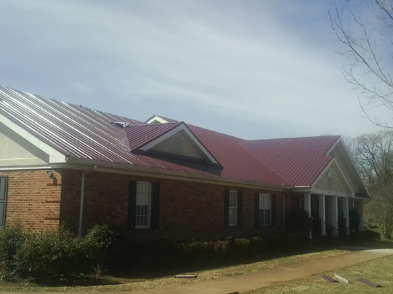 Red metal roof with gabled entries on a long brick building, from a Hail Damage Roof Repair job in Zelienople