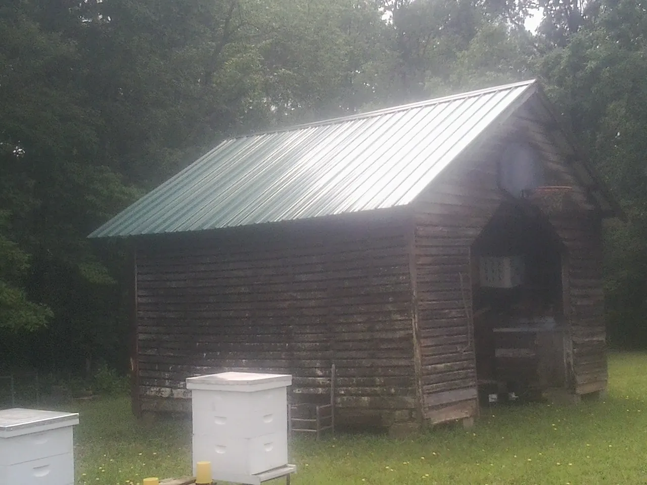 Green metal roof on a weathered barn beside stacked beehives in Zelienople