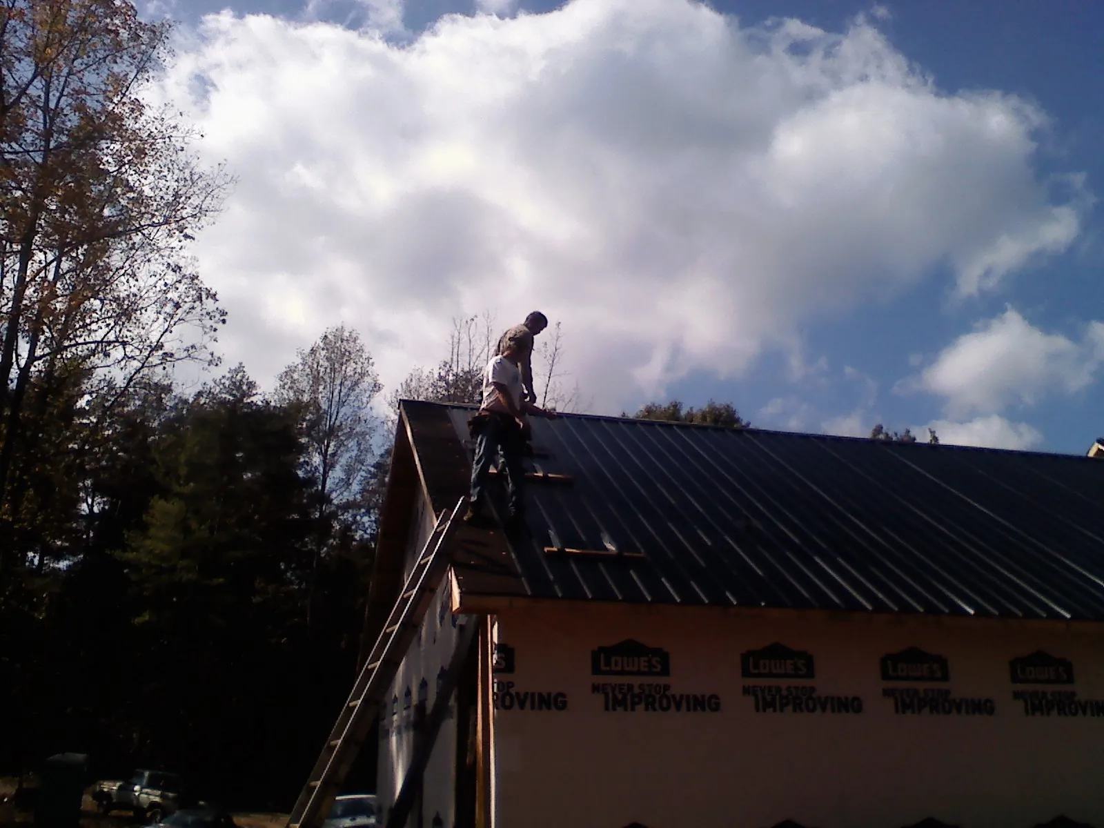 Roofer fastening dark metal panels high against a cloudy sky, from a Roof Inspection job in Zelienople