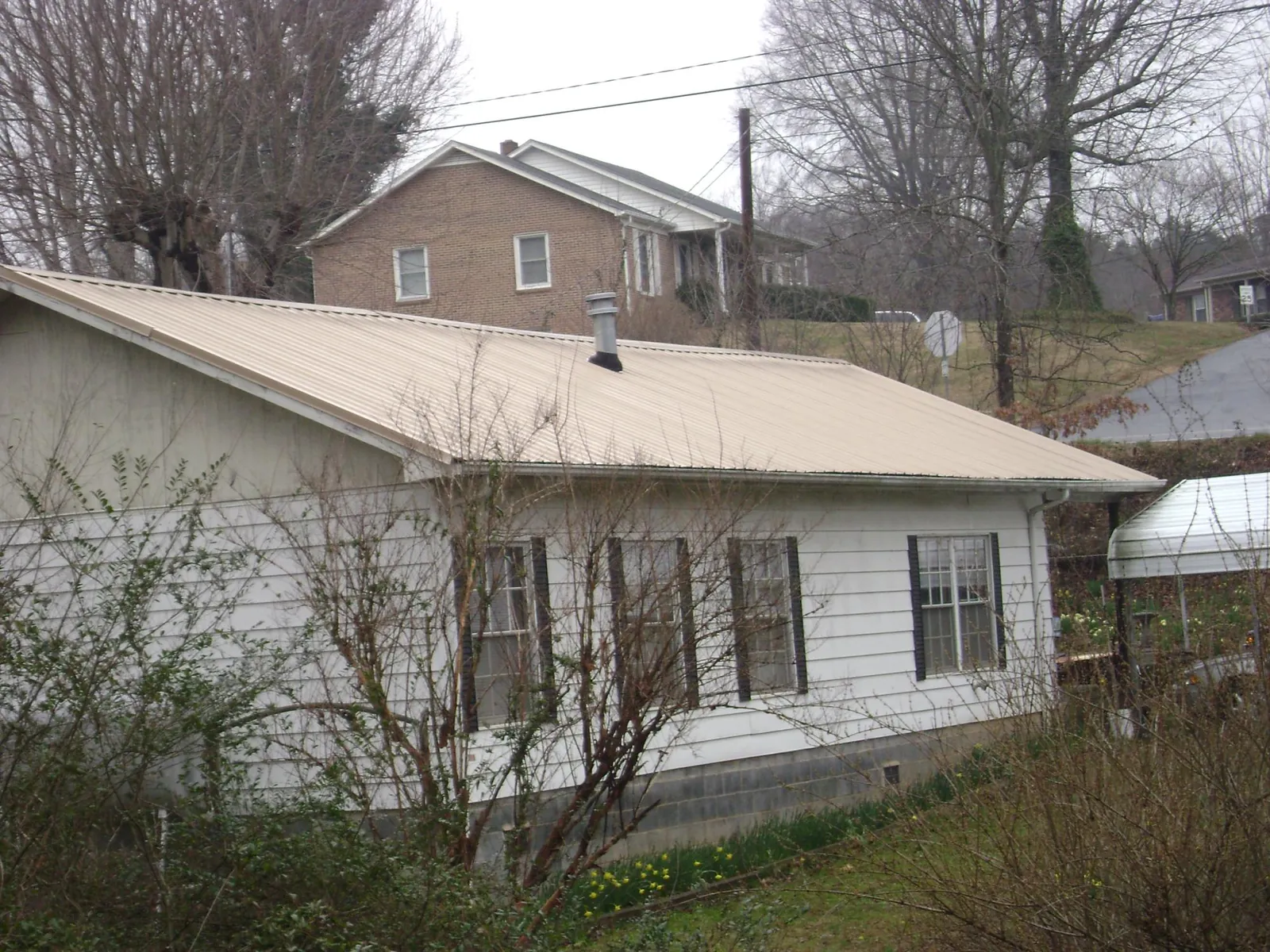Tan metal roof on a white sided house set into a hillside — Commercial Roofing by Roofing Brothers in Zelienople